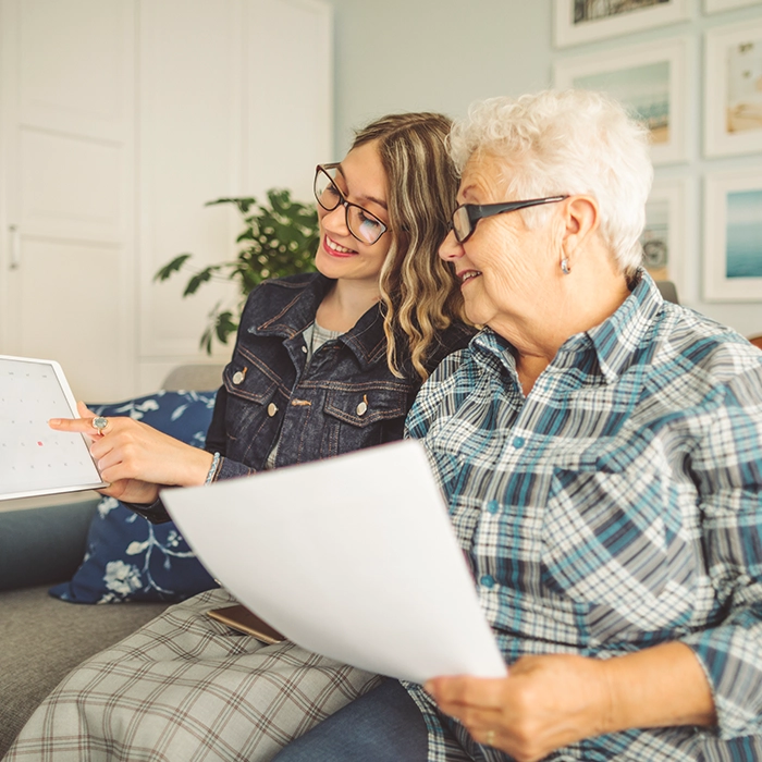 happy senior lady with caregiver pointing at tablet